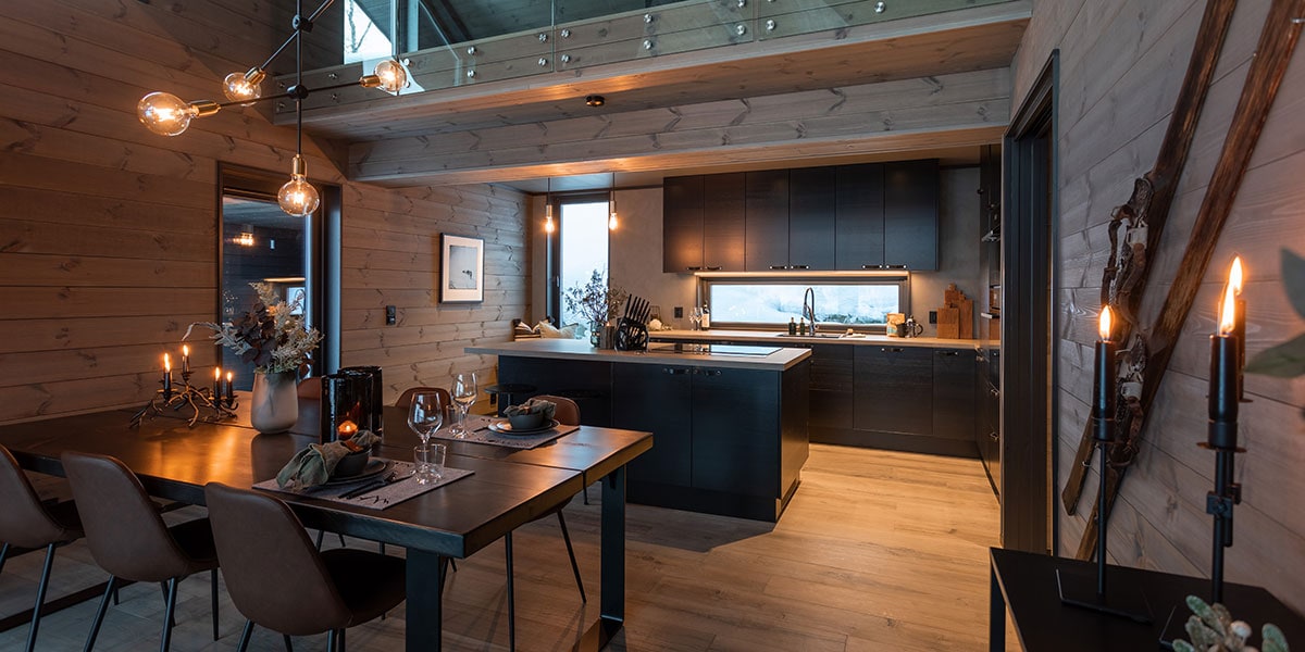 Översiktsbild av köket med mörka fronter och grå betongbänkskiva, bänk med skinn framför fönstret.