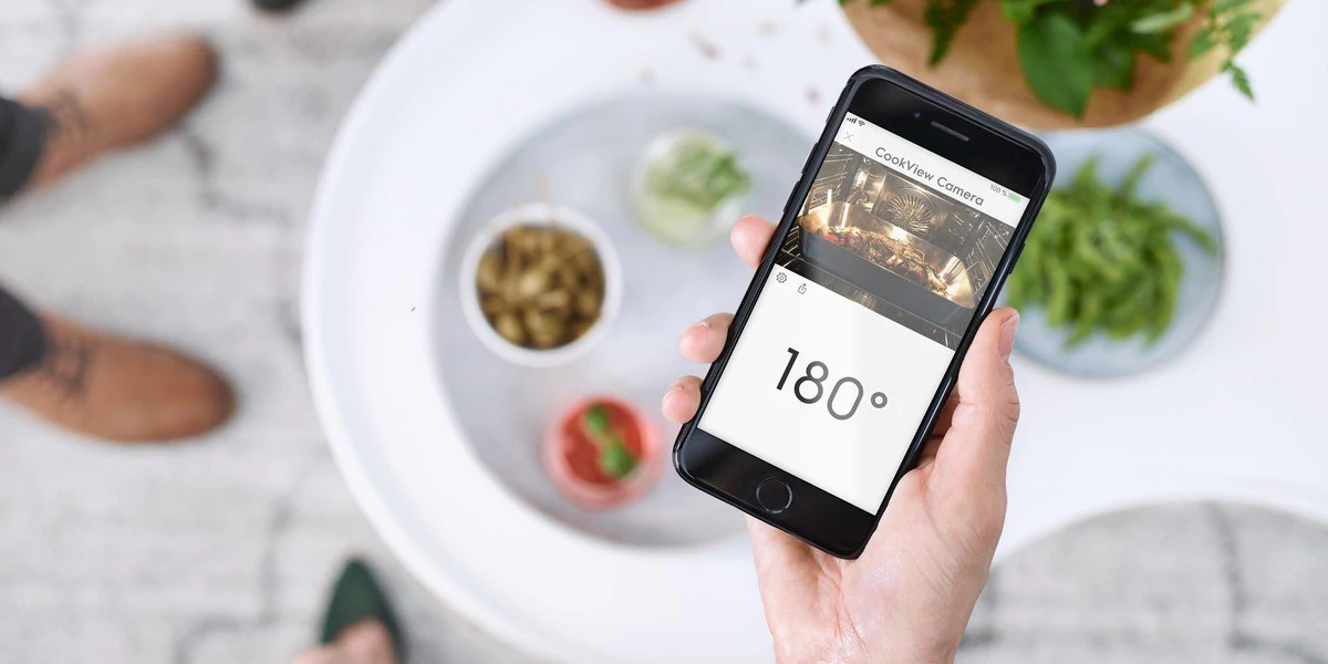 Varför är en ugn med WiFi en bra idé? En hand som håller i en mobil som visar temperatur och streaming av video från insidan av ugnen
