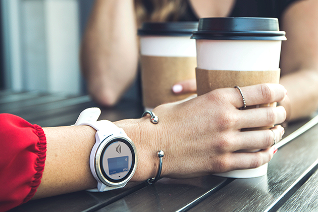 Kontaktlös betalning En hand som håller en kaffekopp med en smartwatch på handleden.