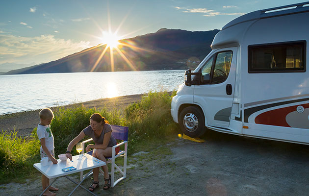 Matlagning på semestern är en utmaning Husbil står parkerad vid vattnet, i solnedgången. En kvinna och ett barn sitter vid ett campingbord utanför