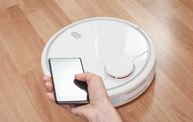 Smart navigeringssystem Hand som håller i en mobiltelefon och en robotdammsugare i bakgrunden
