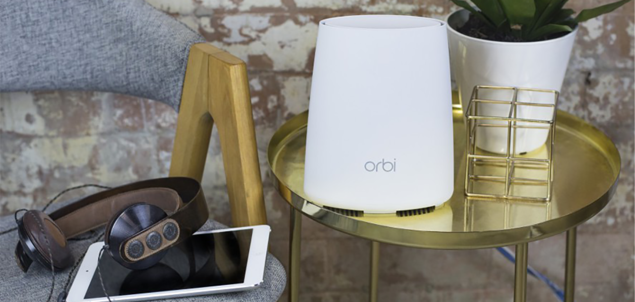 Orbi Mesh är perfekt för det smarta hemmet Netgear Orbi Mesh-enhet på ett bord framför en tegelvägg vid sidan av en stol med en surfplatta och ett par hörlurar