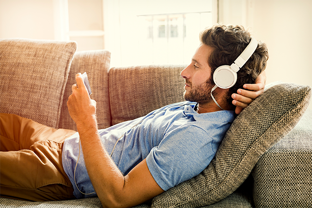 Med en smartphone i handen har du underhållningen vid fingerspetsarna Man ligger på soffan och tittar på sin smartphone