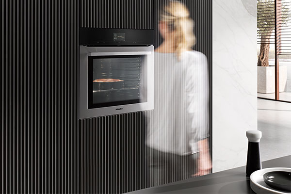 MotionReact – interaktion med ugnen med hjälp av rörelse Miele ugn Generation 7000 med MotionReact passeras av kvinna