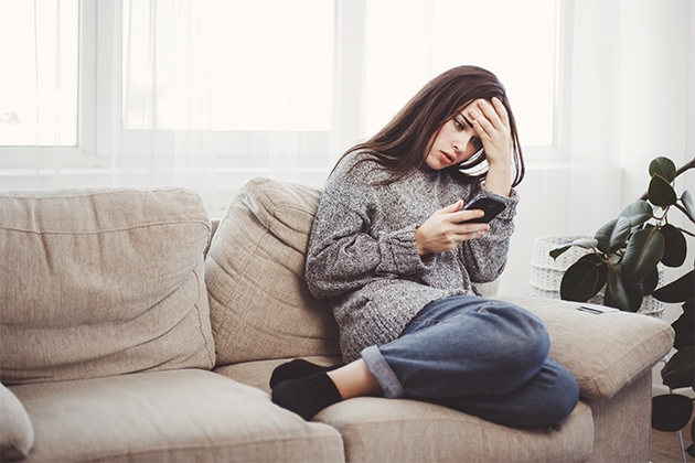 Smarta säkerhetstips för att skydda din mobiltelefon En förtvivlad kvinna sitter på en soffa och tittar på sin mobiltelefon