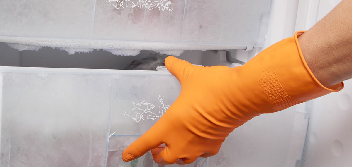 Underhåll av frysen En hand med orange gummihandske som öppnar en igenfrusen frys
