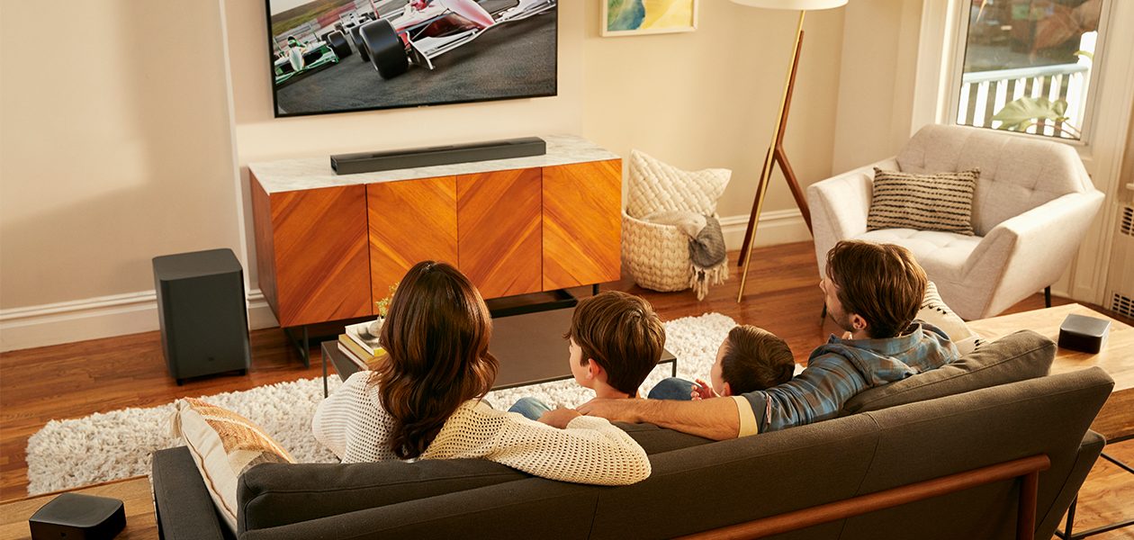 JBL Bar 9.1 soundbar ger dig trådlöst 3D-surroundljud med Dolby Atmos, subwoofer och två trådlösa surroundhögtalare JBL Bar 9.1-anläggning i ett rum där en familj sitter i soffan och tittar på TV