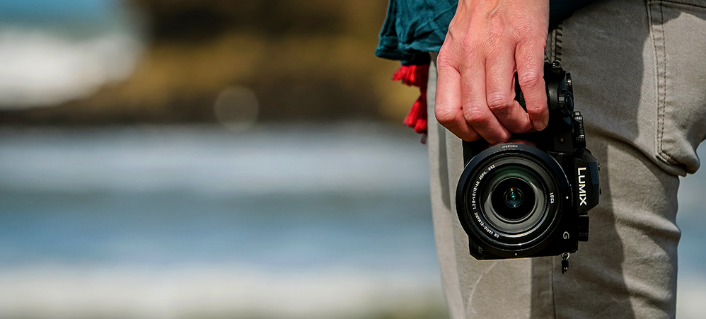 Panasonic LUMIX G90 En hand håller en svart G90-kamera