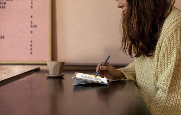 Surface Go 2 med 10,5 tum stor skärm gör det enkelt att hänga med Kvinna sitter på fik med Surface Pen i handen och Surface Go 2 framför sig