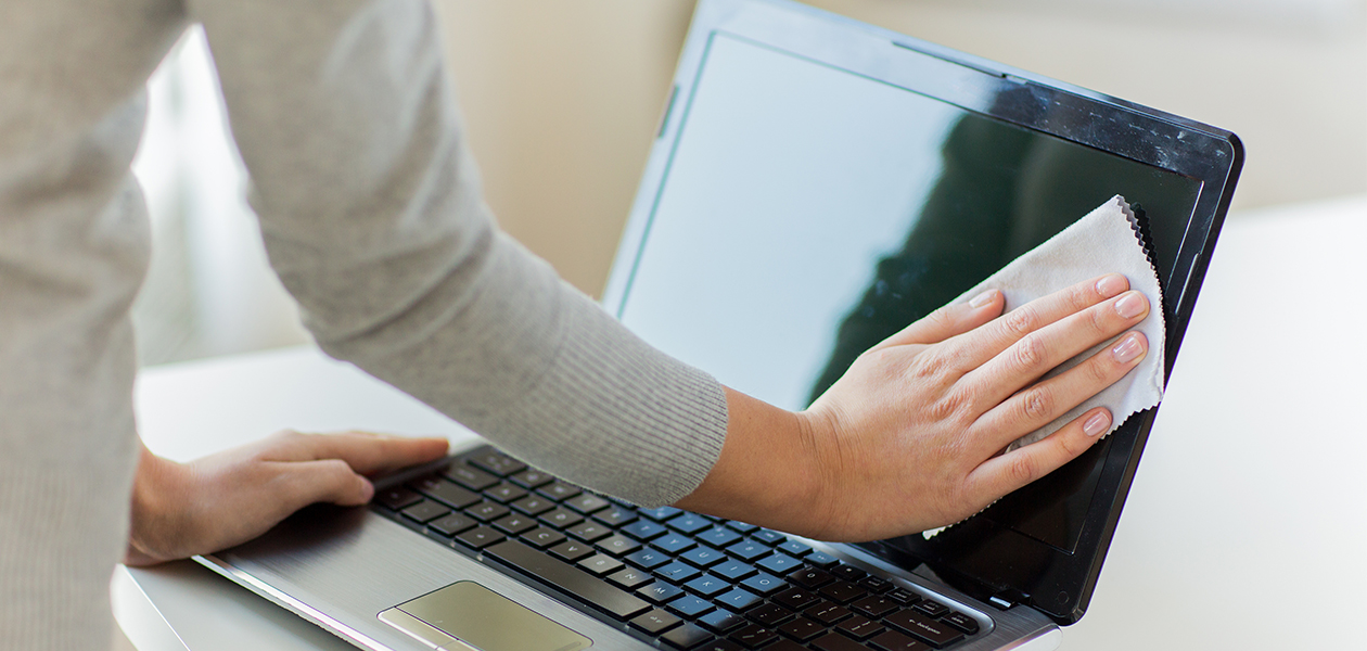 Tips på hur du rengör din laptop En hand som rengör skärmen på en bärbar dator med en vit mikroduk