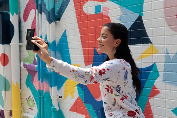 Canon EOS M200 Kvinna som tar selfie med en EOS M200 framför en färgglad vägg