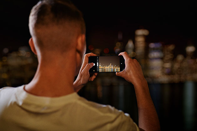 Fånga livets ögonblick med foton och videor med en ny Quad-kamera på 48 MP OnePlus Nord används av en man för att ta bild av en skyline på kvällen