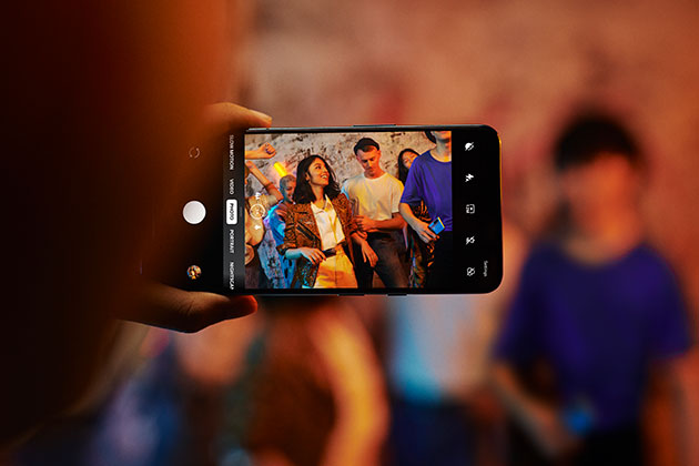 Skärmen ger en vacker visuell upplevelse med en uppdateringsfrekvens på 90 Hz OnePlus Nord i handen på en person, som tar en bild av en grupp människor