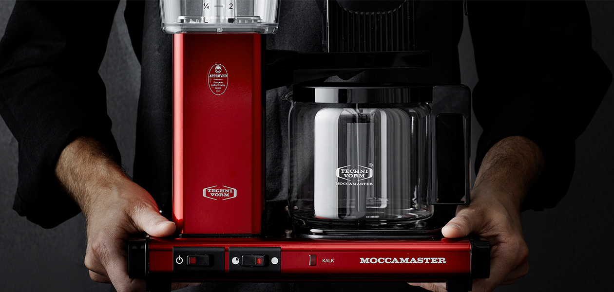 Moccamaster – kvalitet och utsökt kaffe Två händer som håller i en Moccamaster kaffebryggare