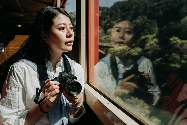 Asiatisk kvinna med en systemkamera som sitter och ser ut genom fönstret på ett tåg