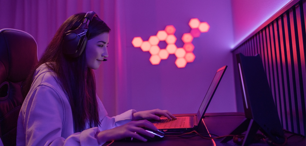 En kvinna med hörlurar som spelar på en bärbar gamingdator