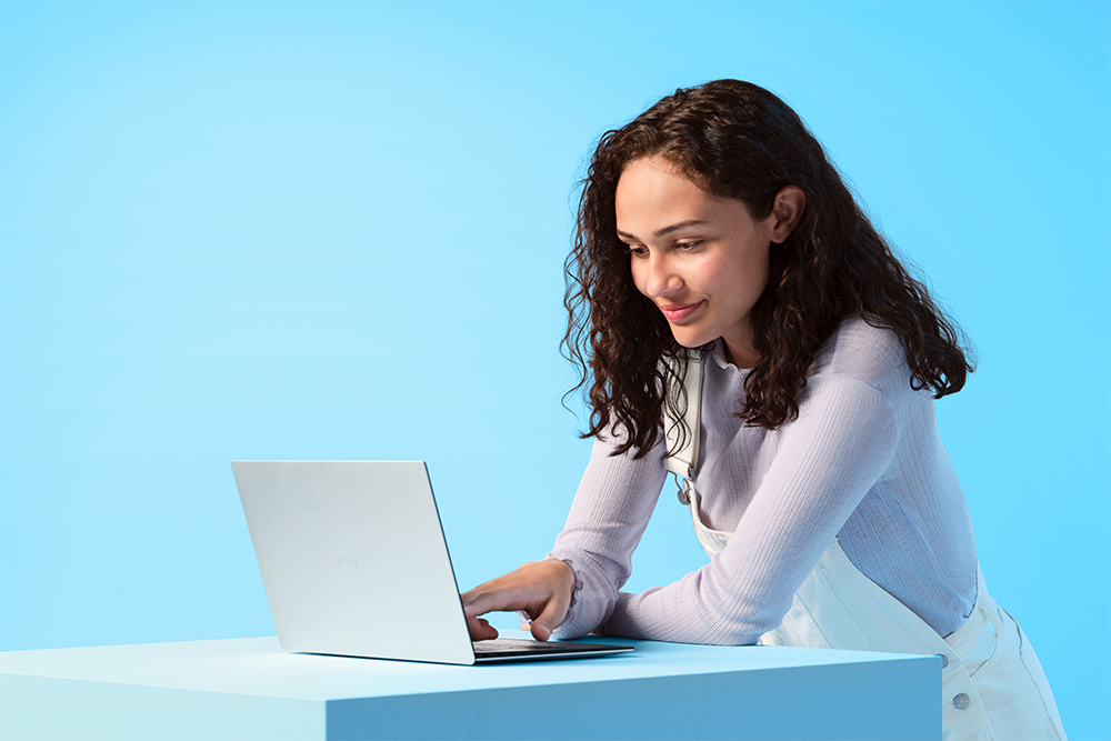 Windows 11 låter dig maximera produktiviteten Kvinna sitter med en Windows 11-dator framför sig på ett blått bord