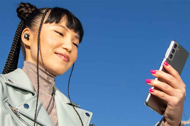 Beats Studio Buds ger dig större trådlös räckvidd och färre avbrott Beats Studio Buds i öronen på en kvinna som håller en mobiltelefonen i handen