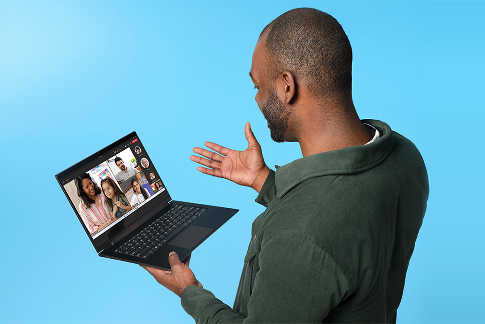 Livet är bättre tillsammans Man i mörkgrön jacka håller en liten Windows 11-laptop i handen och pratar med folk på Teams