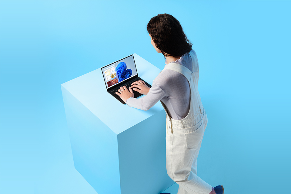 Det du behöver – när och var du behöver det. Kvinna står med Windows 11-laptop på en blå kub