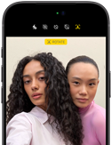 iPhone 18 Pro, i färgen svart, sedd framifrån, två modeller som poserar framför kameran för att visa Center Stage-skärmkameran