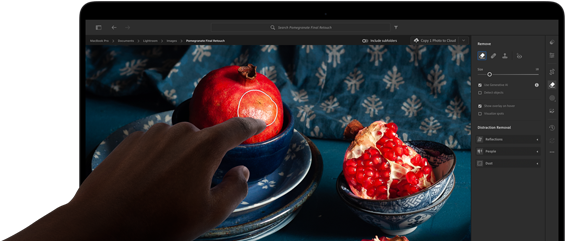 MacBook Pro med PROLED XDR-skärm som visar ett stilleben med granatäpplen samt blå keramikföremål och textilier, en hand sträcks ut mot skärmen för att interagera med bilden