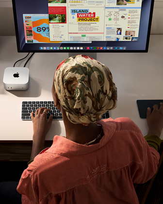 En person skriver vid ett skrivbord med en Mac mini med Studio Display ansluten, Magic Keyboard, Magic Trackpad och olika föremål