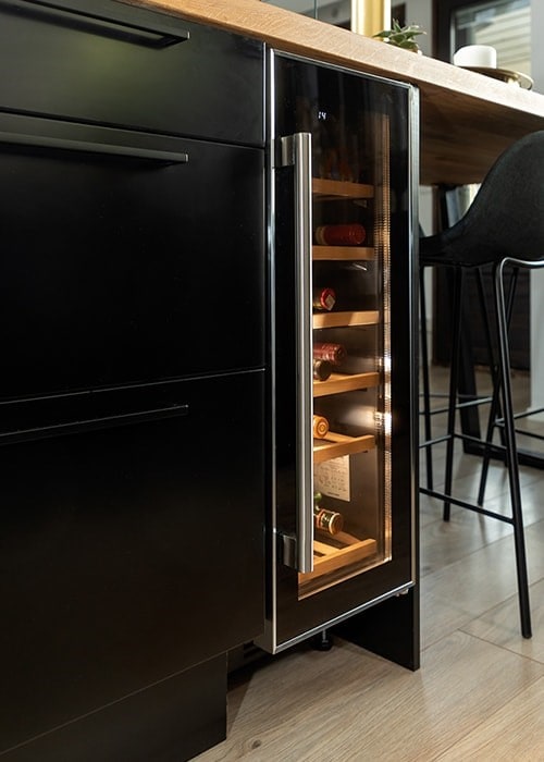 En vinkyl är placerad på köksön vid sidan av svarta kökslådor och med en barstol på andra sidan. 