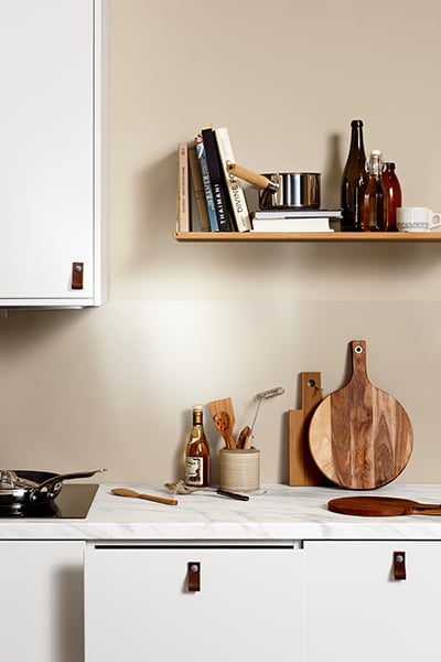 Vitt kök från Epoq Core Classic White med läderhandtag, en hylla med böcker och skärbrädor i trä.