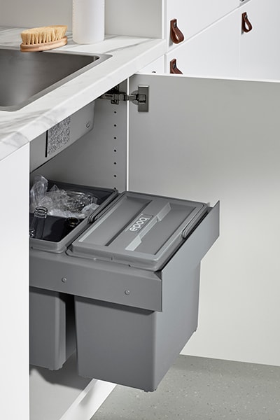 Öppen kökslucka under diskbänken visar ett sopsorteringssytem i grå färg. 