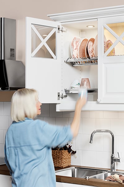 Kvinna ställer upp ren disk i ett glasskåp i ett vitt kök från Epoq.