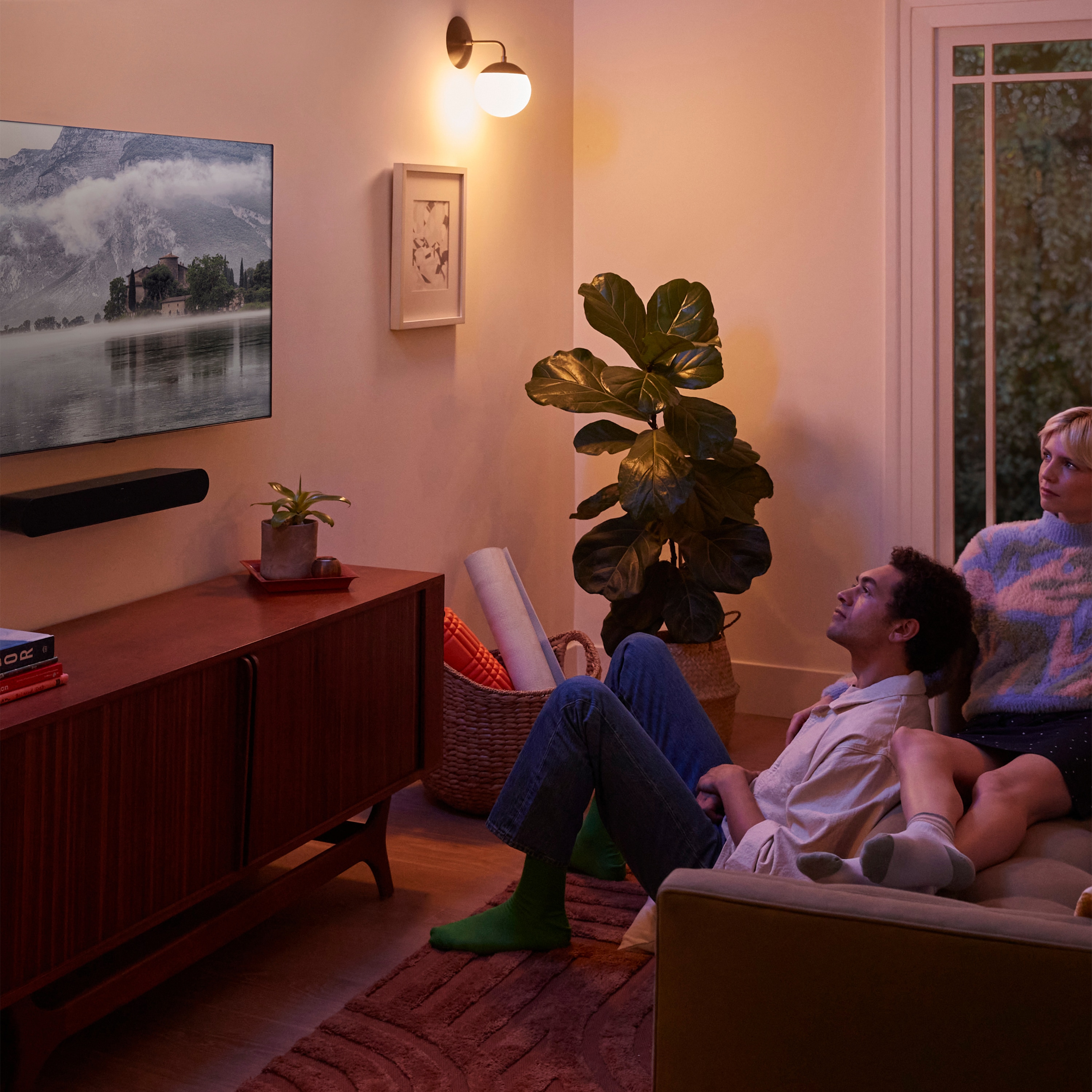 Två män i ett vardagsrum som tittar på TV med en soundbar fäst på väggen under den