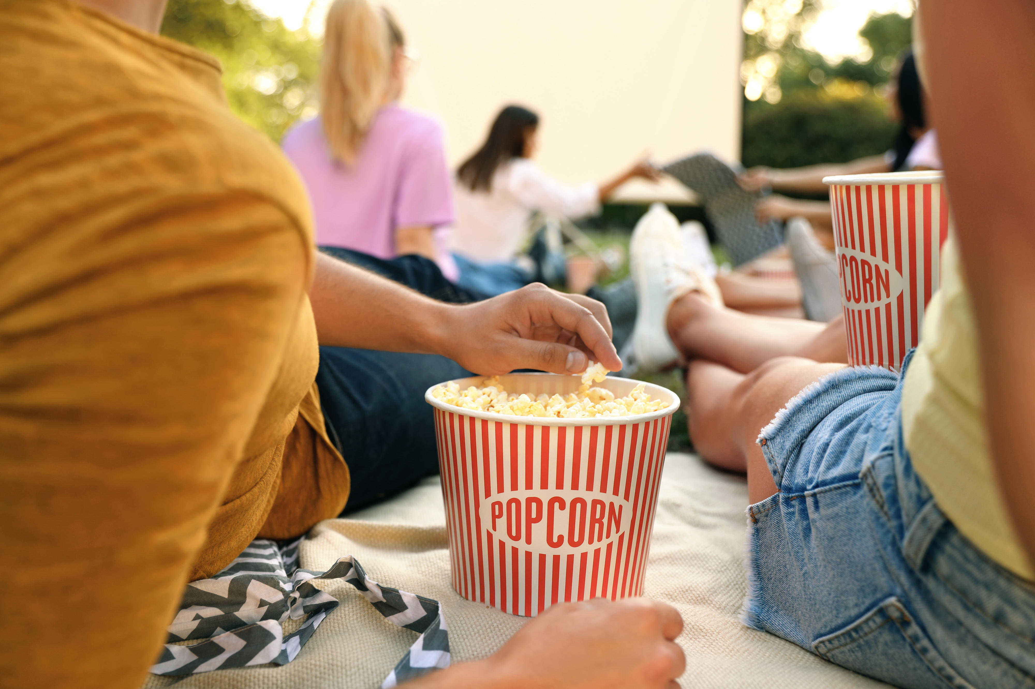 Par som äter popcorn och som tittar på en skärm utomhus med flera andra i en trädgård