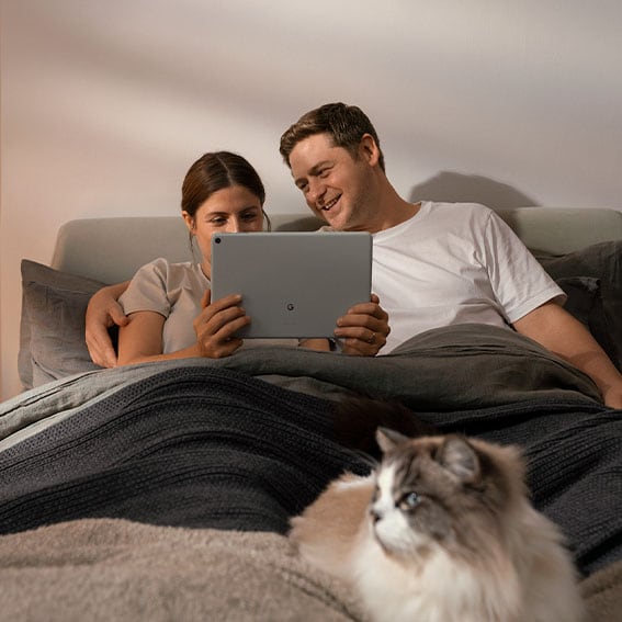 Kvinna och man i sängen tittar på Google TV på Google Pixel Tablet