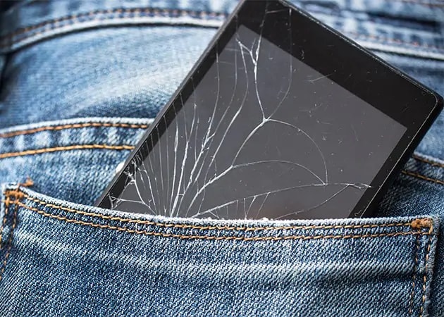 En mobiltelefon med en sprucken skärm i en jeansficka.