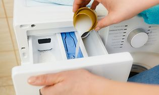 Person häller upp flytande tvättmedel i en tvättmaskin, närbild på facket för tvättmedel och händer. . 
