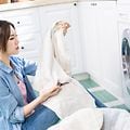 Kvinna sitter på golvet i en tvättstuga framför tvättmaskinen och inspekterar ett lakan.
