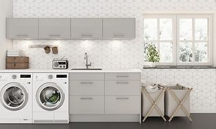 Epoq: Tvättstuga i grå/beige nyans med två tvättkorgar, tvättmsakin och torktumlare vikta handdukar i en hög och en radio. 