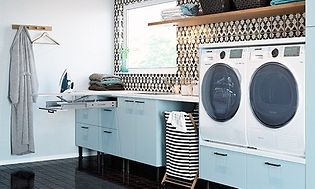 Epoq: Tvättstuga med ljusblå lådfronter, en randig tvättkorg, tvättmaskin, torktumlare och en utdragen strykbräda.