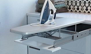 Epoq: En strykbräda som dragits ut från en låda, med ett strykjärn uppställt på. I bakgrunden syns en hög med vikta kläder.