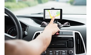 En GPS fäst på instrumentbrädet i en bil och en arm som sträcker sig fram och pekar på den.  