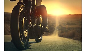 Motorcykelpå en lång väg genom öknen med solnedgång i bakgrunden. 
