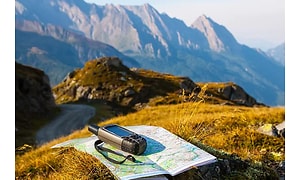 En GPS och en karta placerad på en gräsplätt omgiven av höga berg och en fascinerande natur. 