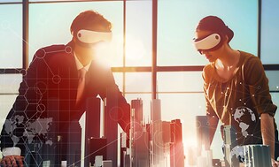 En man och kvinna står med VR-glasögon på sig och ser på något slags prototyp av en stad, på ett kontor med stora fönster.