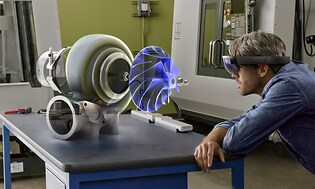 Man står i en verkstad och har på sig AR-glasögon så att han ser ett extra tillbehör i lila färg på maskinen som han ser på. 