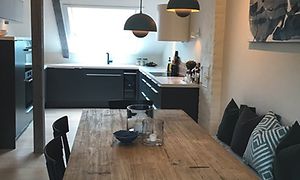 Epoq kök i mörkgrå stilren design anpassat för rummet med lutande väggar. Köksbord i trä i förgrunden. 