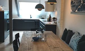 Epoq kök i mörkgrå stilren design anpassat för rummet med lutande väggar. Köksbord i trä i förgrunden.