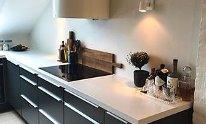 En vit bänkskiva i Avonite med mörkgrå kökslådor under och en induktionshäll. Vid sidan på bänken står det några flaskor.