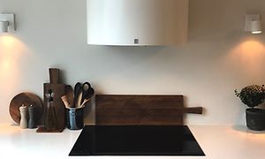 Kökslådor i mörkgrå färg, induktionshäll och en stor vit rund köksfläkt ovanför. Köksredskap står vid sidan av.