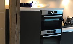 Kylskåp i mörkgrå färg och integrerad ugn, två stycken, en träbjälk vid sidan och blå glas ovanpå kylskåpet.